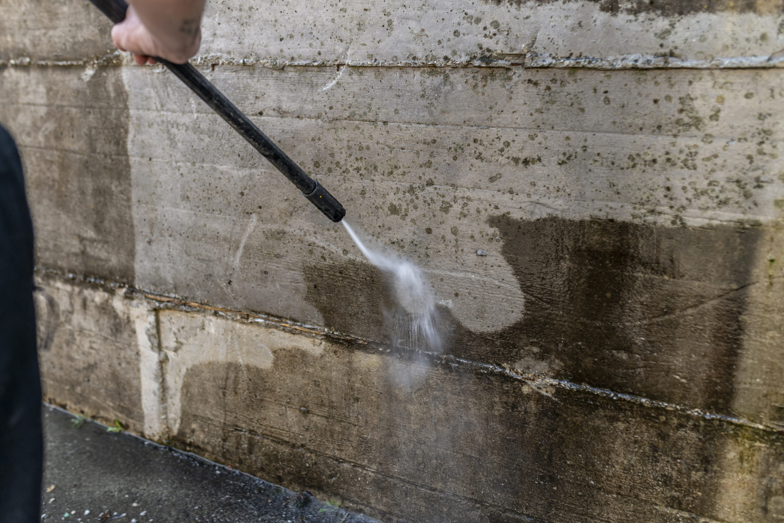 A person is cleaning a concrete wall with high-pressure water blasting.