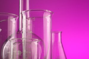 A group of flasks for scientific purposes sit next to each other against a neon purple background.