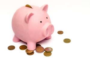 A pink piggy bank is sitting atop some coins that are spread out on a white background.