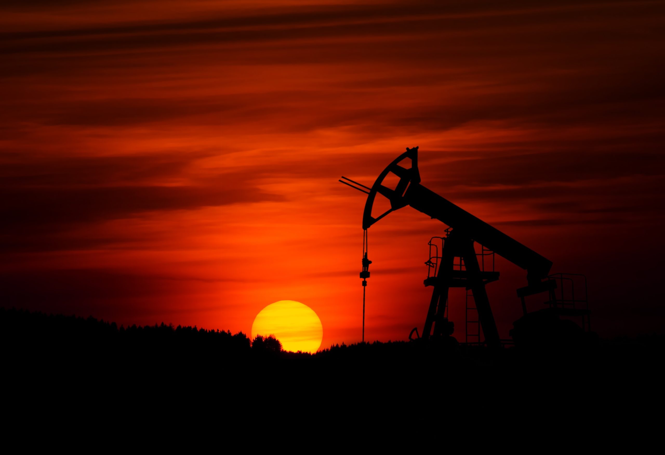 A pump-jack is mining crude oil against a sunset.