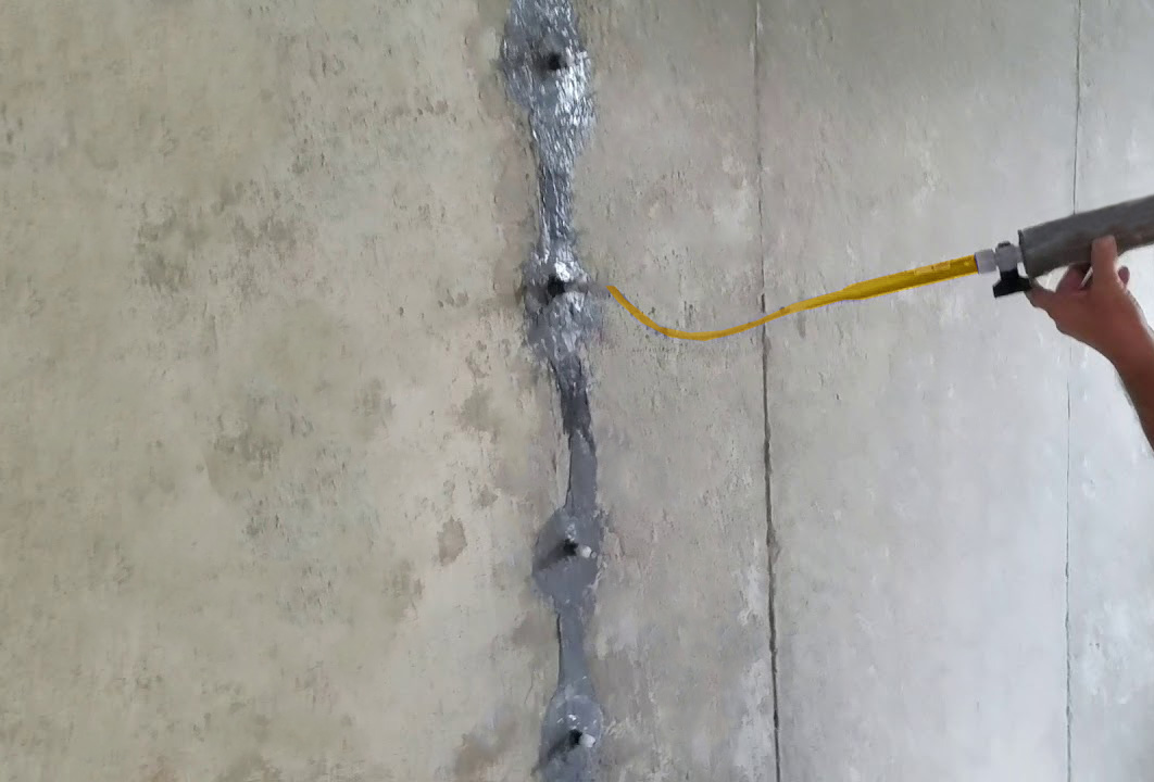 A construction worker is inserting injection product into a concrete crack.