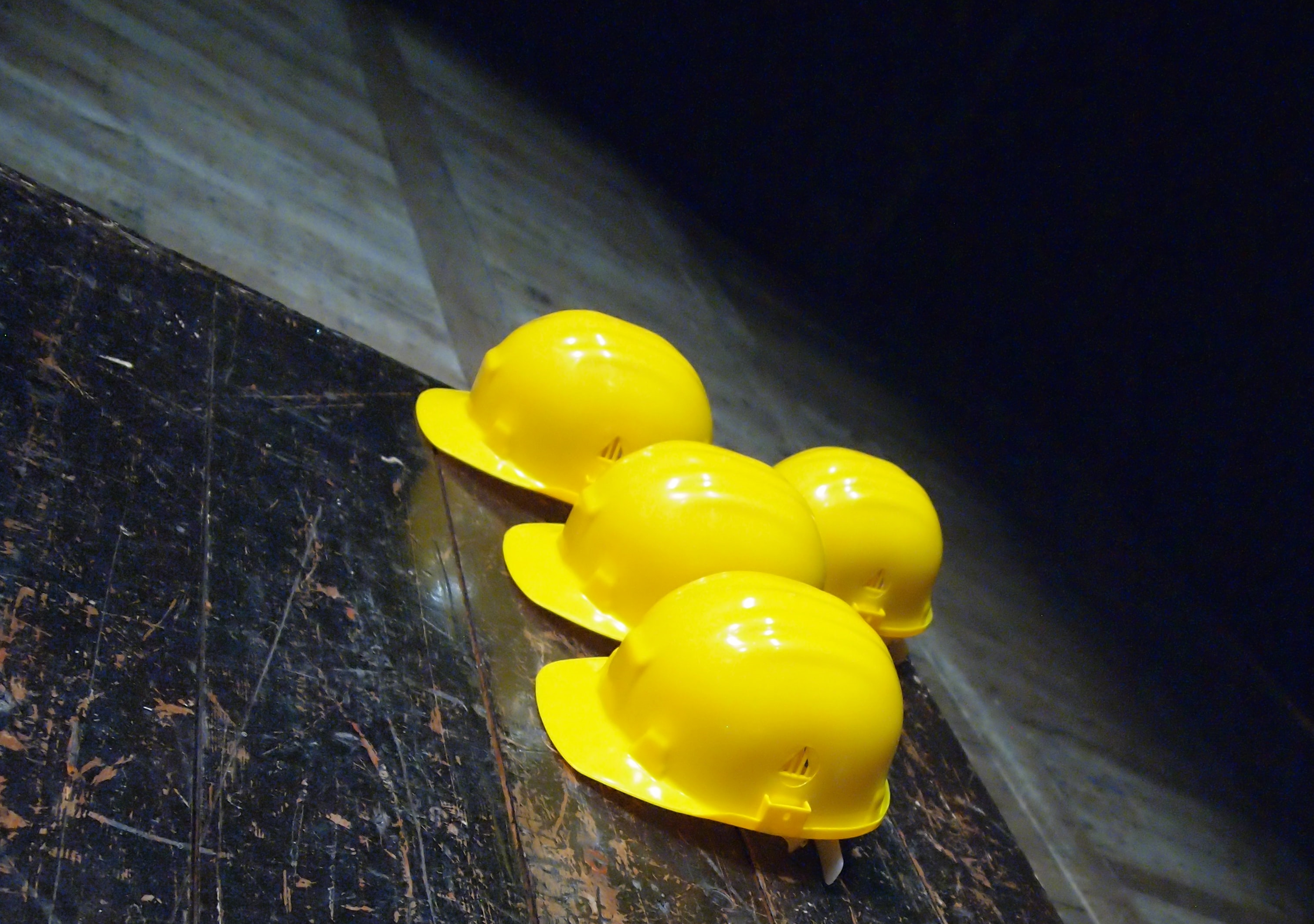 A bunch of toy yellow hard hats are grouped together overtop dark flooring.