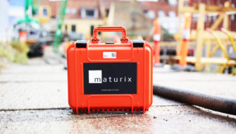 The orange carrying case for Maturix Smart Concrete Sensors is sitting on pavement near a construction site.