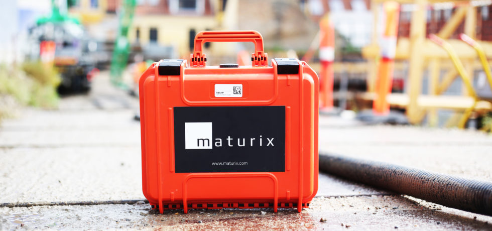 The orange carrying case for Maturix Smart Concrete Sensors is sitting on pavement near a construction site.