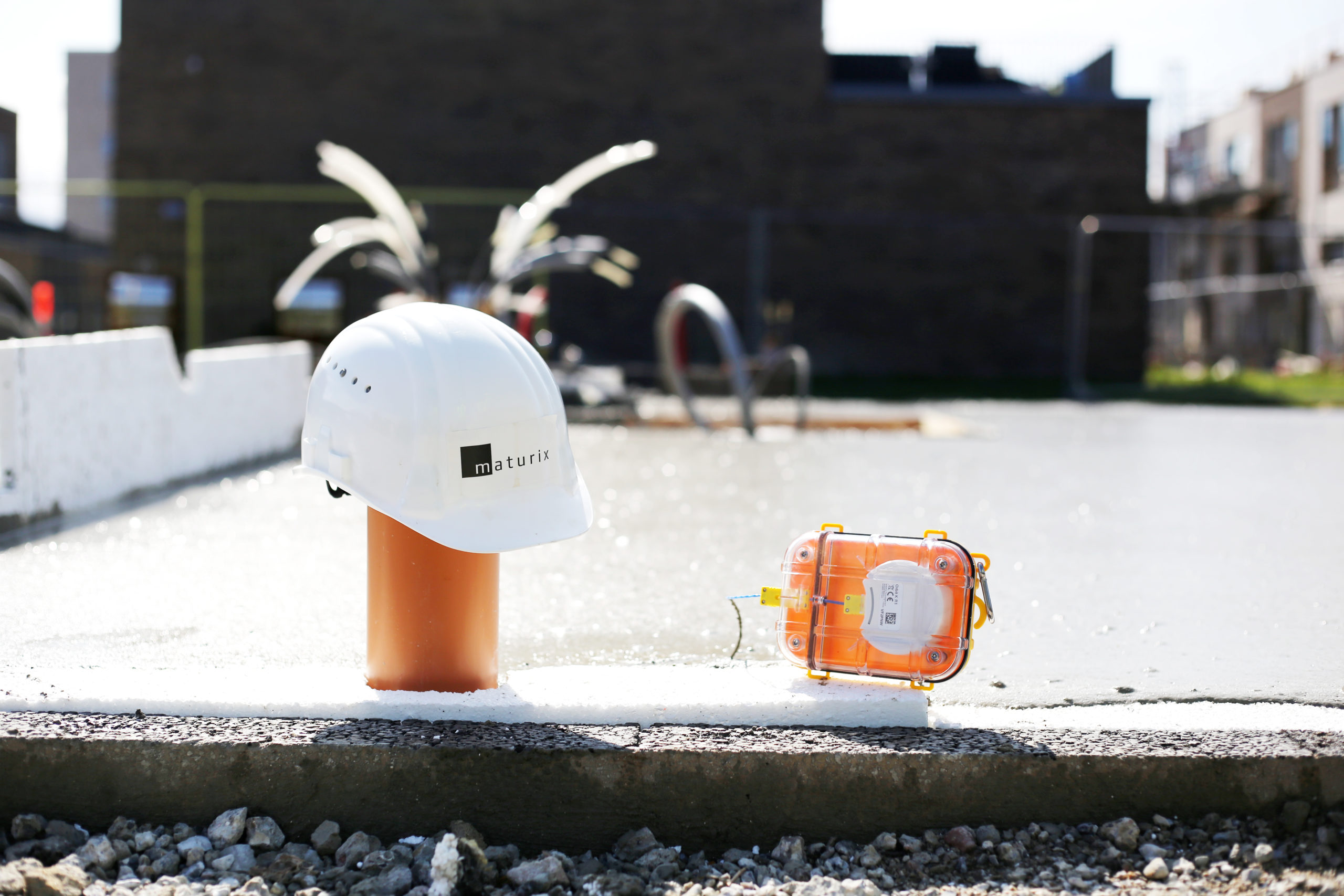A white hard hat is sitting on an orange pole next to a Maturix Smart Concrete Sensor with sparks shooting up from behind.