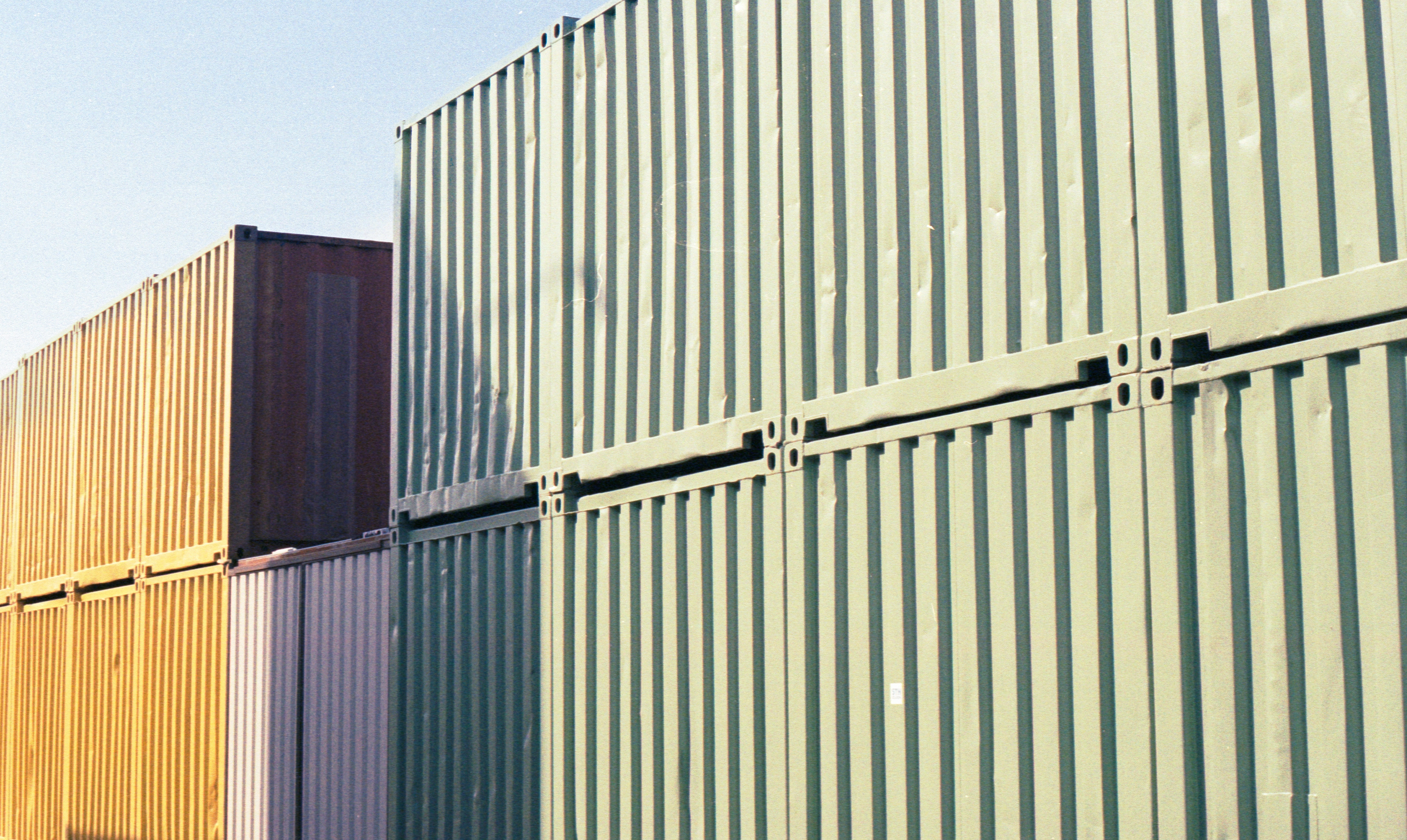 Two shipping containers on top of one another sit in the sun next to another pair of shipping containers.