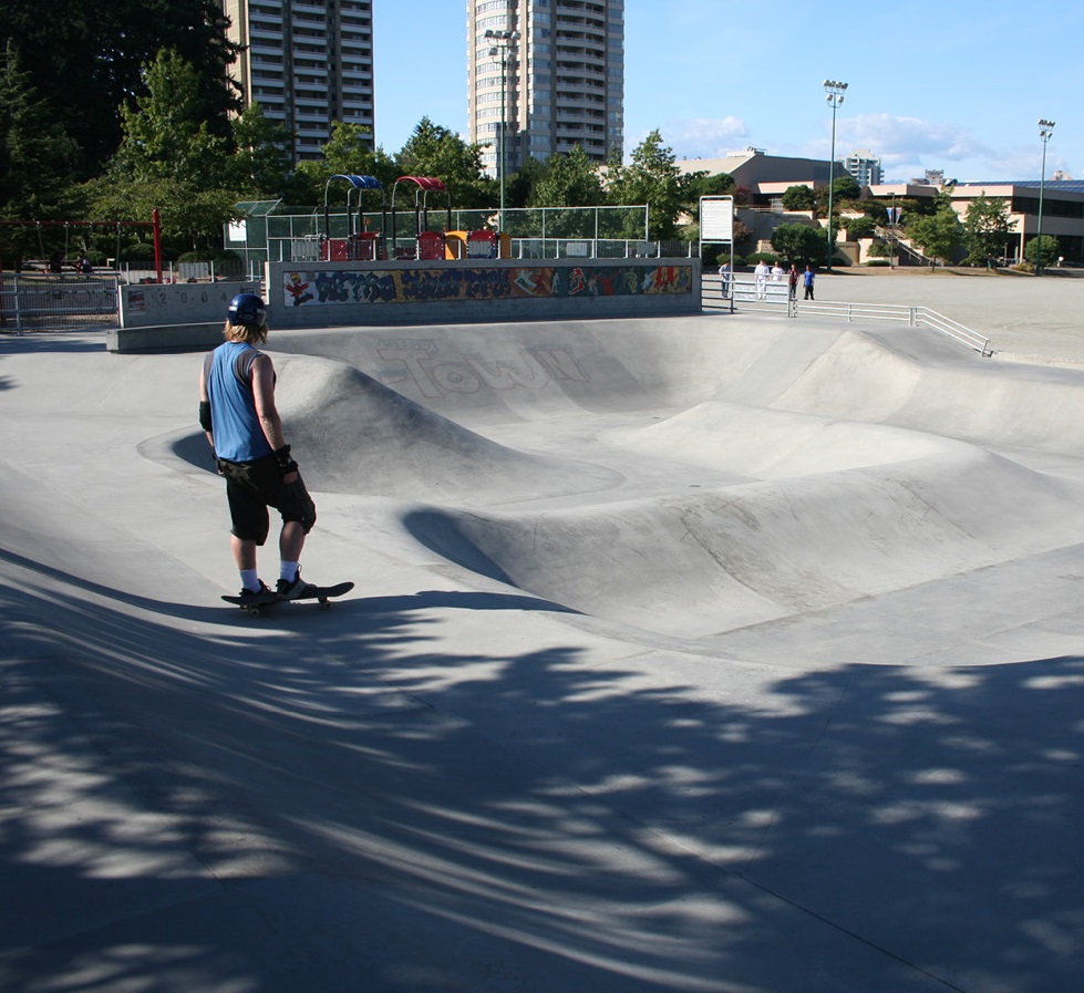 A young blonde-haired man stands on top of his skateboard before using it to traverse across the concrete treated with Hard-Cem.
