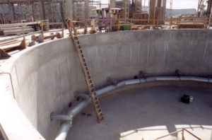 A ladder is resting against the inner wall of a concrete tank for a wastewater treatment tank.