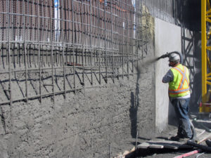 A construction worker is spraying Hard-Cem shotcrete over a steel reinforced area.