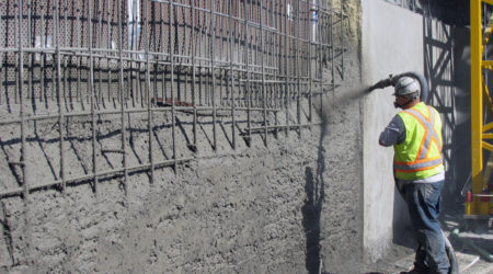 A construction worker is spraying Hard-Cem shotcrete over a steel reinforced area.