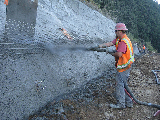 A construction worker is spraying shotcrete while standing on a slope.