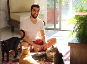 Man in white tee is surrounded by four cats.