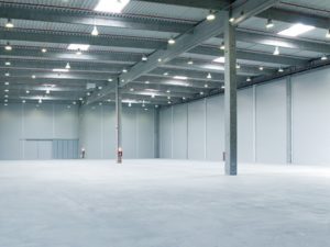 Spotless concrete floor is lit up from numerous lights above in a giant warehouse.