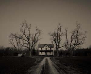 A haunted house sits in-between several barren trees.
