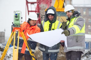 Three civil engineers at a worksite in winter are looking at a chart.