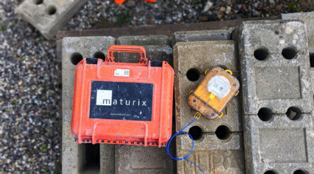 A Maturix Sensor and its case are laying next to each other on concrete blocks in a worksite.