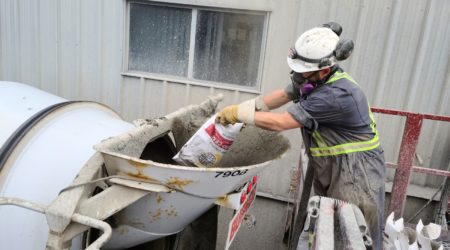 A construction worker is adding Hard-Cem into his concrete mix during batching.