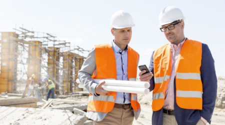 Two male engineers look at a mobile phone to see the Maturix platform at a construction site under a clear, sunny sky.