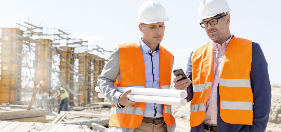 Two male engineers look at a mobile phone to see the Maturix platform at a construction site under a clear, sunny sky.