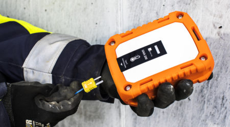 A construction worker is holding a Maturix Sensor in one hand and a thermocouple cable in the other hand.