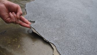 A building professional is lifting a torn membrane to see the reason for the waterproofing membrane failure.