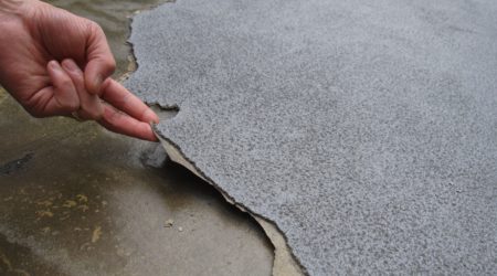 A building professional is lifting a torn membrane to see the reason for the waterproofing membrane failure.