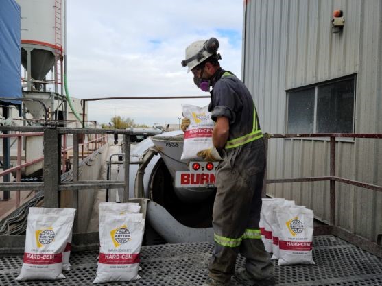 A construction worker is lifting a Hard-Cem bag to put it into a ready-mix truck.