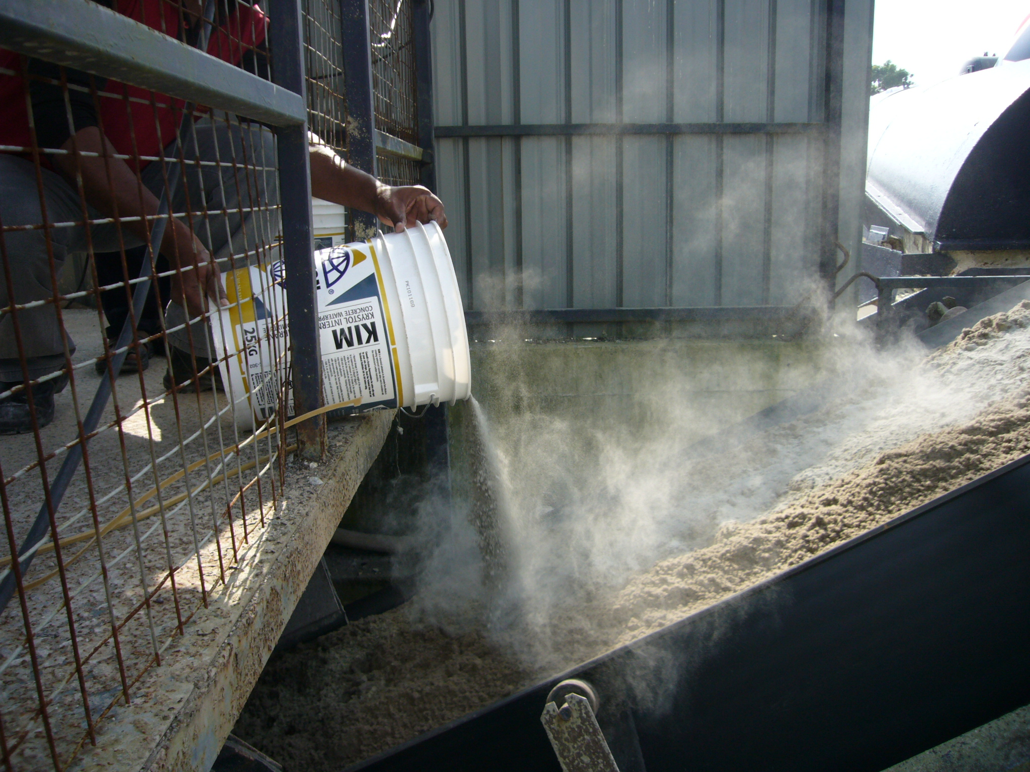A construction worker is pouring a pail of KIM into a concrete mix.