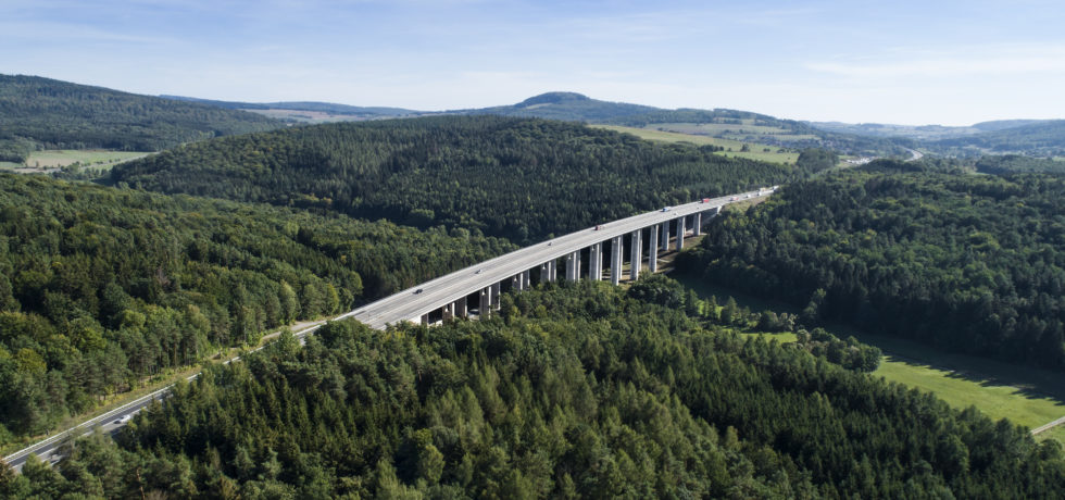 A panoramic aerial view of a highway bridge among vast amounts of greenery.