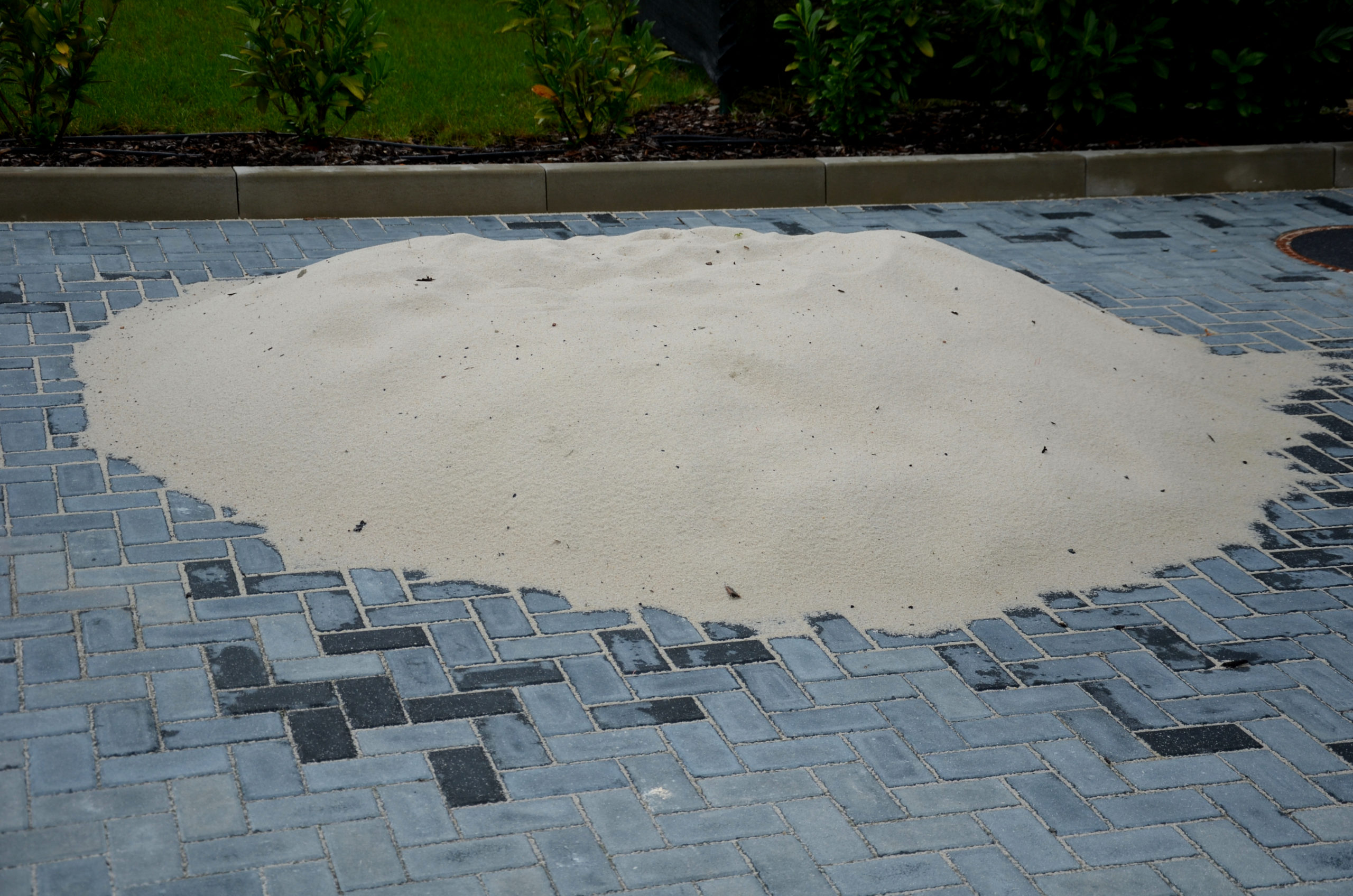 A pile of silica sand rests on concrete pavement.