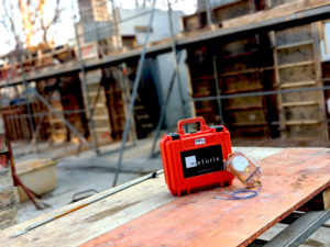 A Maturix Sensor is leaning against an orange case with the Maturix logo on top of wooden beam in a worksite.