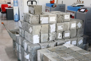 A pile of concrete cube samples are waiting to be tested for compressive strength in an industrial room.
