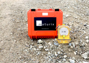 A Maturix Sensor is leaning back on an orange case with the Maturix logo on gravel.