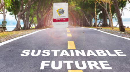 A road is surrounded by grass, trees, and one lawn chair has the words "Sustainable Future" on it, and it leads to an illuminated Hard-Cem package, which is meant to help sustainable construction.