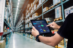 A warehouse owner is holding a tablet to see how successful the warehouse business has been.
