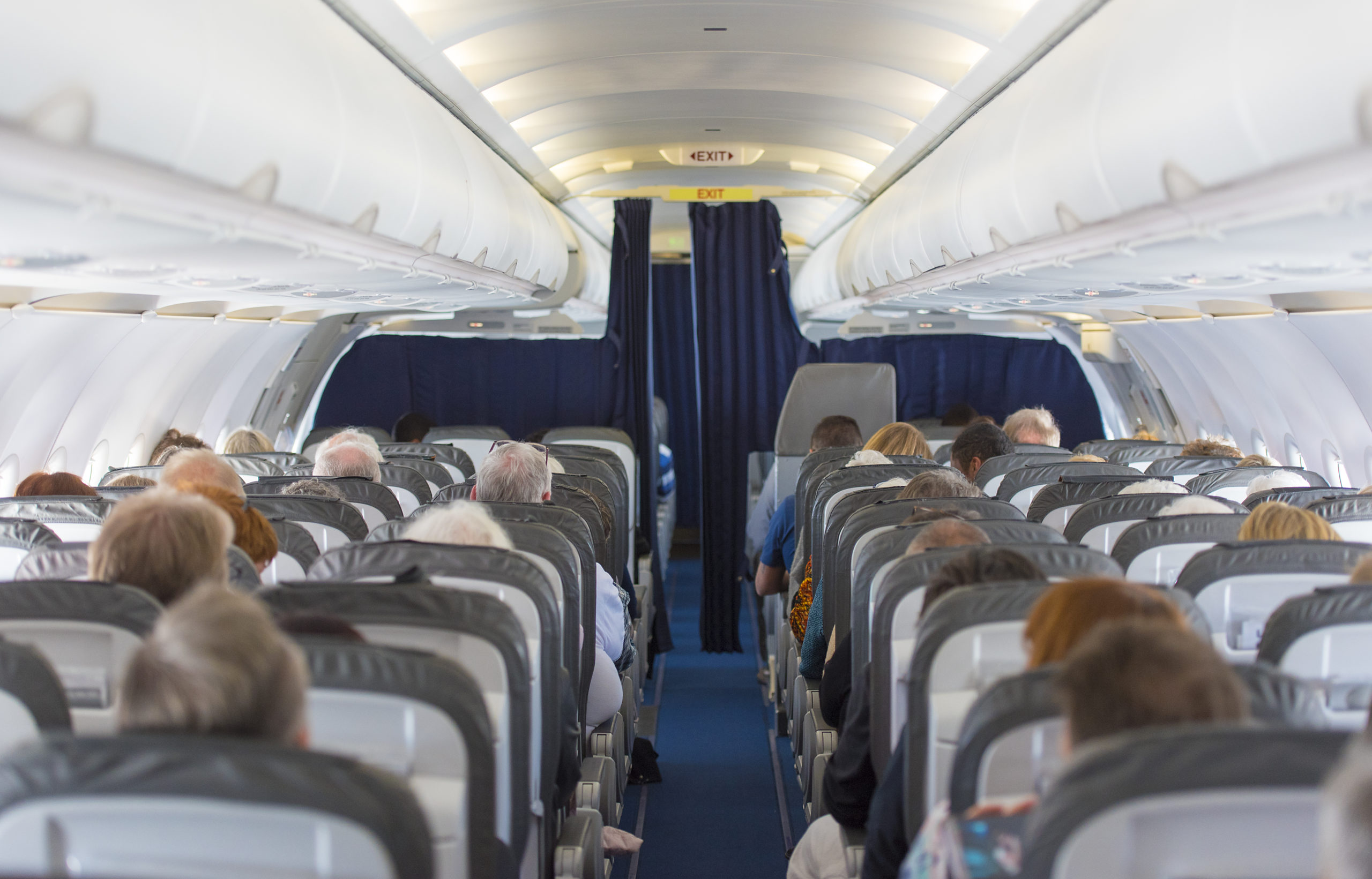 A commercial aircraft cabin is full of passengers sitting as they wait to be flown to their destination.