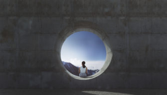 A young woman is sitting in a circular concrete opening and looking out at mountains.