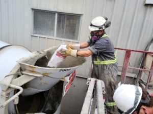 A construction worker is throwing in a bag of Hard-Cem admixture into a concrete mix during batching.