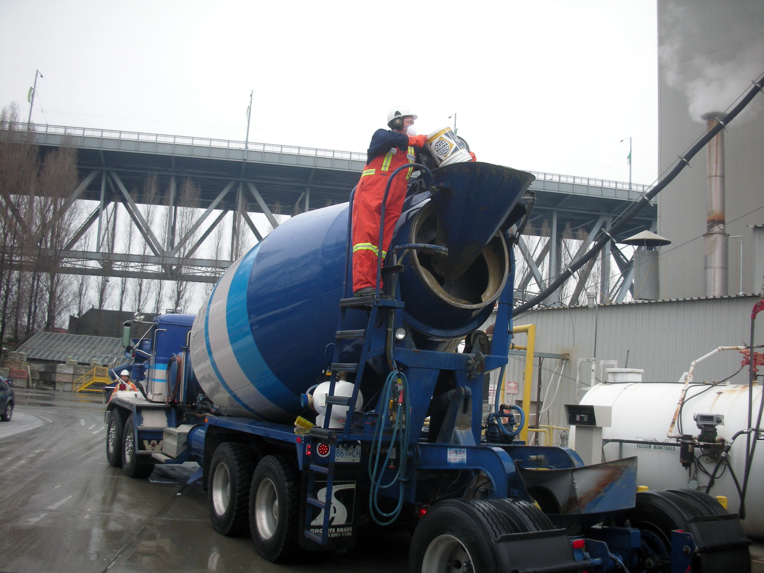 A construction worker is adding KIM admixture into a concrete mix during batching.
