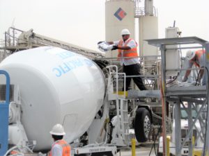 A worker is adding KIM, a crystalline waterproofing admixture, to the concrete in a ready-mix truck during batching.
