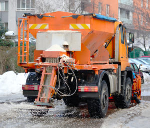 To provide freeze-thaw resistance, a snow-plowing and road-salting truck is doing maintenance work on a road during winter.
