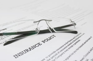 A pair of glasses with black temples sits on top of insurance policy papers for construction.