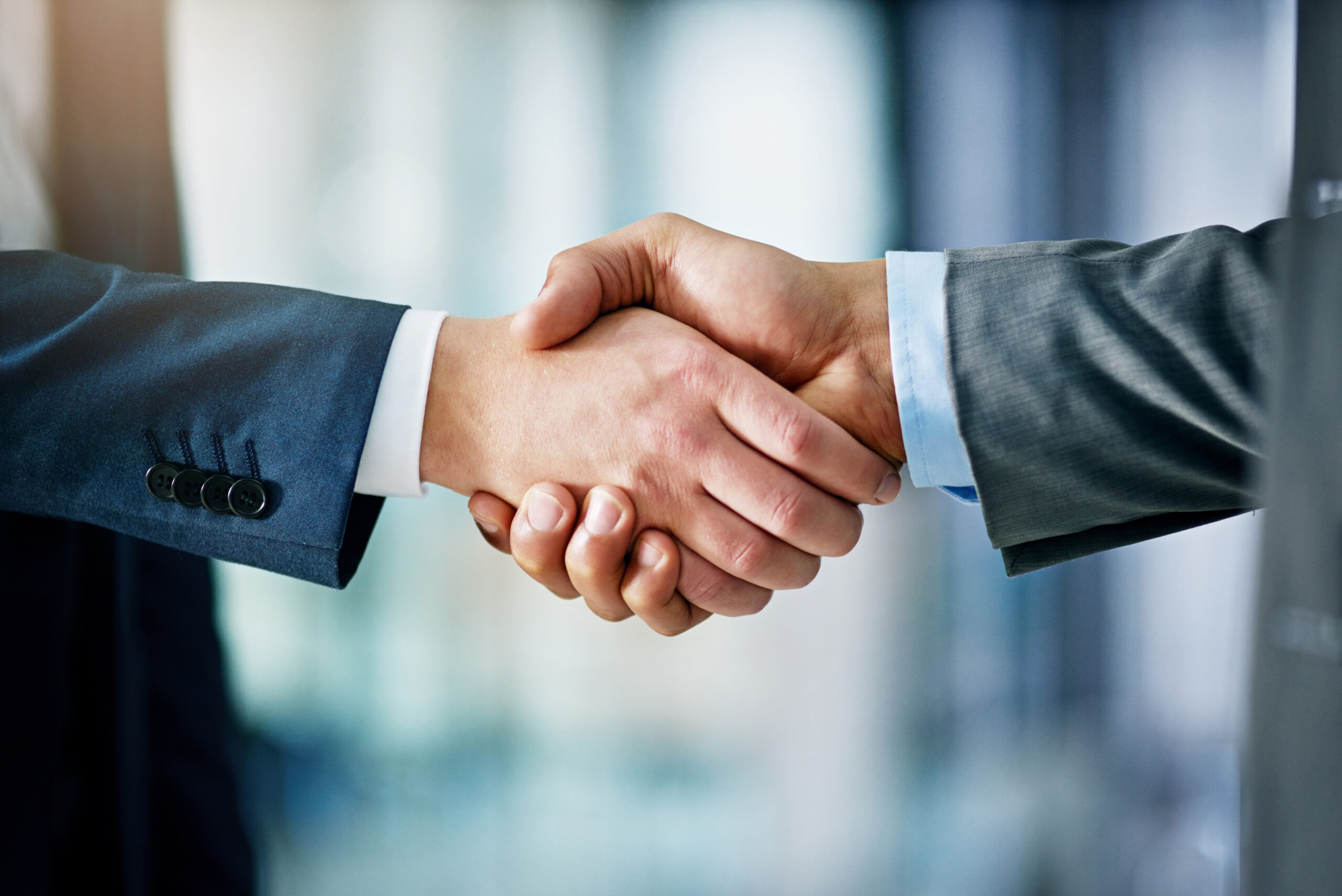 The hands of two business leaders are clasped in a handshake against an out-of-focus background.